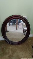 Full view of round mahogany framed wall mirror resting against a wall on carpeted floor.