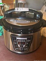 Front and side view of the Tristar Power Cooker Model WAL-4 with digital control panel, showing stainless steel body, locking handle on lid, and cook settings buttons.