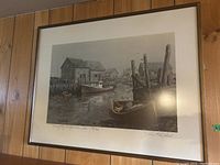 Photo of the framed limited edition print showing the foggy harbor scene with boats and signature of the artist, mounted on wood-paneled wall.