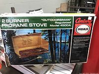 Boxed Century Primus Model 4500A 2 burner propane stove, showing front with outdoor scenic graphics and branding.