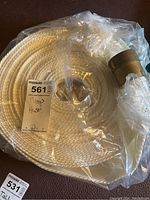 Photo showing coiled white woven pump hose with brass fittings, wrapped in plastic with label indicating 'Pump Hose'.