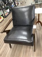 Front view of a black faux leather accent chair with dark wood armrests and legs, showing the seat and backrest.