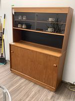 Front view of solid wood cabinet with sliding glass doors on top and sliding wood doors below.
