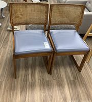 Front view of two matching wood frame chairs with cane backs and blue vinyl seats, showing overall condition and style.