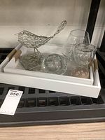 Full view of metal bird sculpture, clear round glass tealight holder, round glass bud vase, small sand timer, and white serving tray with rope handles