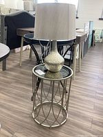 View of lamp on top of metal frame side table with mirrored top on showroom floor