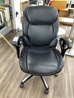 Front view of the black faux leather swivel office chair showing padded backrest, seat, and armrests with white stitching.