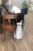 Wood tiered plant stand alongside metal plant stand holding a plant, white metal watering can, and metal fish-themed coat hook leaning on the floor.