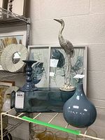 Photo of the lot showing two framed botanical prints, blue ceramic vase, blue ceramic candle holder, green glass jar, and metal crane figurine.