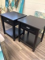 Pair of black wood and laminate side tables shown side by side.