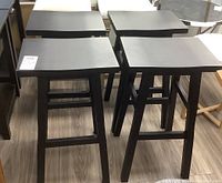Four matching black wooden stools arranged in two rows of two, showing top and side views.
