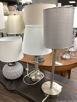 Photo showing three table lamps with different bases and shades placed on a wooden surface.