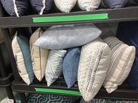Eight assorted throw cushions stacked on black shelves showing variety in color and style.