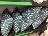 Four blue and white geometric patterned down-filled throw cushions arranged upright on a rack.