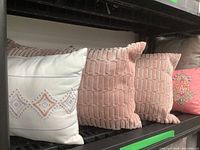 Four throw cushions on a shelf showcasing various colors and textures including white with embroidery and pink cushions
