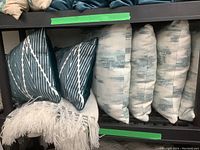 Six throw cushions and cream fringed throw blanket arranged on a shelf showing different patterns and condition.