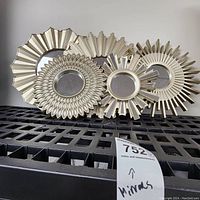 Four plastic framed decorative wall mirrors with intricate sunburst and floral designs placed on a black surface.