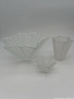 Front view of three frosted glass vases with ruffled edges on neutral background.