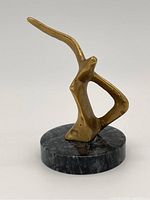 Angle view of the brass and stone abstract sculpture showing the smooth brass form and stone base.