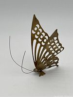 Side view of brass butterfly sculpture highlighting detailed cut-out wing patterns and wire antennae.
