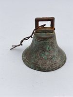 Image of an aged copper alloy bell showing oxidation and green patina on the exterior with a square rusted handle and attached wire loop.