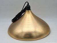 Close-up photo of the single brass-tone conical pendant light shade showing its smooth brushed surface and attached black cord and socket.
