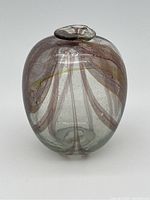 Front angled view showing signature purple and amber peacock feather pattern on clear glass vase with rounded oval shape and flared mouth.