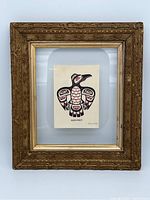 Front view of gilded ornate frame housing Haida Raven art card under glass, showing overall condition, design, and dimensions.