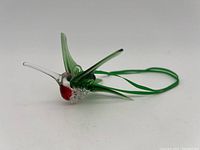 Glass hummingbird figurine, showing clear beak, green wings, red head detail, and textured glass body from side angle