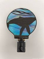 Front view of the glass whale night light showing decorative round glass panel with whale silhouette and ocean background on black plastic base with switch
