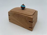 Front angle view of the wooden lidded box showing dovetail joints, rounded lid, and colorful knob