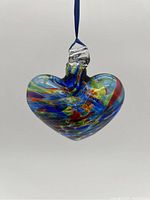 Front view of the Kitras art glass heart ornament showing multicolored swirl pattern with blue ribbon hanging.