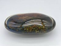 Top view of large oval art glass piece showing iridescent internal patterns in metallic colors.