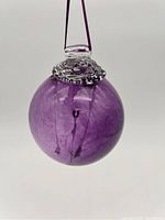 Clear view of spherical purple glass bauble with attached hanging ribbon