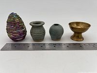 Full lot of four small pieces including glass egg, two ceramic vases, and brass chalice with a ruler for scale