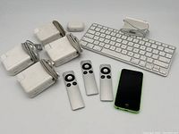 Lot contents: four MagSafe chargers, three Apple TV remotes, Apple wired keyboard, green iPhone 5C, headphone case, power adapter