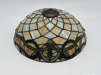 Dome-shaped stained glass lamp shade on white background, showing beige, cream, and green glass pieces with metal top fixture.