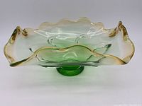 Green uranium glass pedestal dish with wavy amber-tipped edges, shown from side angle