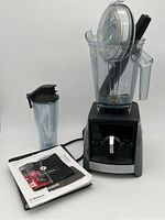 Vitamix blender with 64 oz container, smaller to-go container, manual and recipe book displayed together.