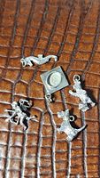Clear view of five antique and vintage sterling silver charms including seahorse, graduation cap with coin, two dogs, and Cupid on brown surface