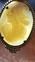 Close-up front view of the antique hand carved cameo pendant showing profile of a woman's head in an oval cameo set in a decorative metal frame.