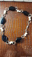 Full necklace arranged to show black onyx stones, pearls, and textured linking rings on patterned brown surface