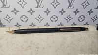 Black PVD Cross mechanical pencil lying horizontally on cloth with Louis Vuitton pattern in background, tip extended in photo lstimg_01j8xbym7kffjb485ma421dbg6