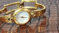 Front view of Esq ladies watch showing gold tone round case, mother of pearl dial, single gold tone hand, and black stone crown. Gold tone bracelet links visible.