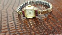 Full view of ladies antique Fortress watch showing gold-tone flexspan bracelet, rectangular watch face with garnet bezel.