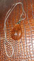 Photo of amber pendant and foxtail chain on a textured brown surface showing the overall size and shape