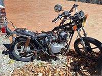 Side view of heavily used 1979 Kawasaki KZ400H LTD motorcycle frame with visible engine, rear suspension, wheel, and handlebars in outdoor setting.