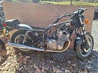 Side view of the motorcycle frame showing engine, exhaust pipe, partially assembled front and rear suspension, missing seat and fuel tank.