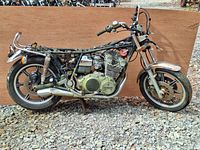 Full side profile of the vintage partially dismantled Yamaha XS750SF Special motorcycle frame with engine and wheels on gravel background.