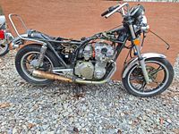 Side view of partially disassembled vintage Suzuki GS550 motorcycle showing engine, frame, rear wheel, exhaust, and missing seat.